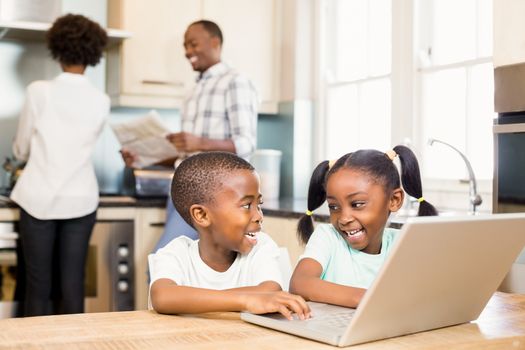 Siblings using laptop against parents in kitchen