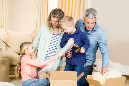 Portrait of happy family opening boxes in living room