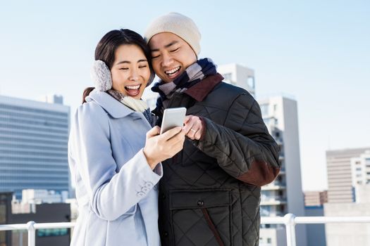 Cheerful couple looking at the smart phone against the building