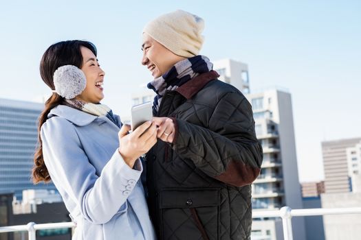 Couple laughing while holding smartphone against building