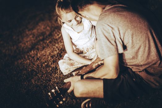 Dad Playing Guitar For His Daughter. Little Girl Learning Guitar Playing. Dark Sepia Color Grading.