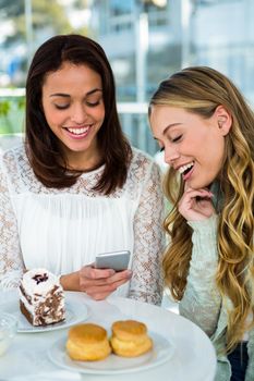 two girls watch a phone while eating