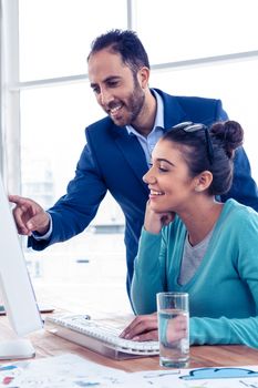 Happy businessman explaining to coworker over computer at creative office