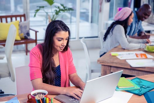 Beautiful businesswoman using laptop while working with colleagues in creative office