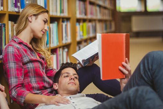 Student reading book while lying on his classmate in library