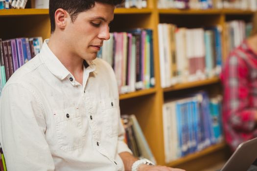 Concentrated male student working on floor in library 