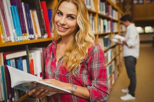 Smiling female student reading book in library