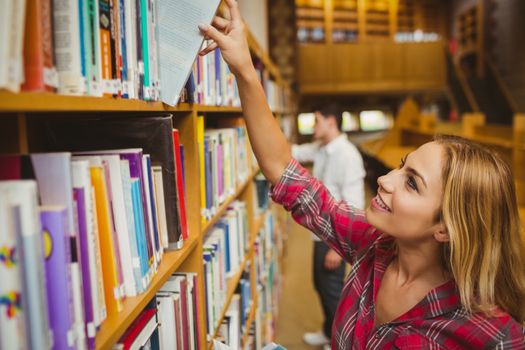 Smiling female student taking book in library