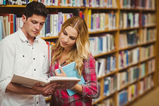 College students reading book together in library 