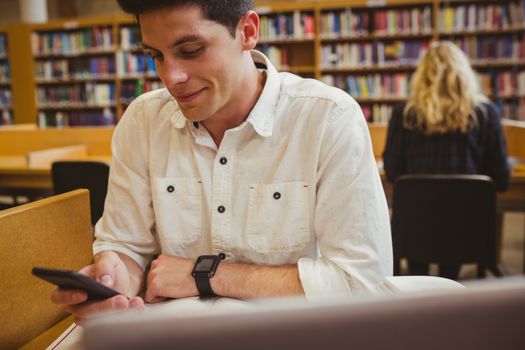 Smiling student using his smartphone in library