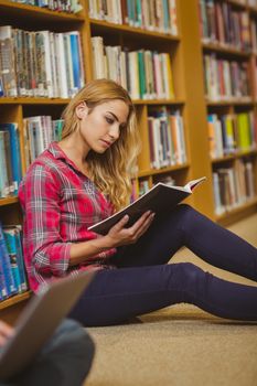Concentrated female student working on floor in library