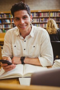 Smiling student using his smartphone in library