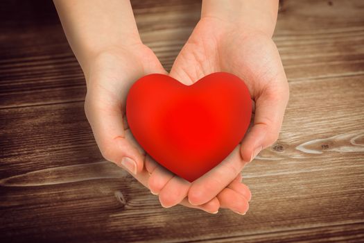 Hand showing heart against wooden floor