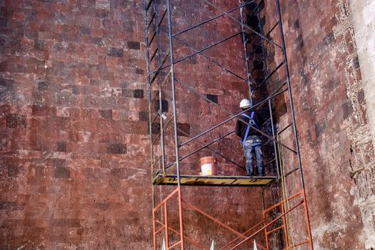 Construction worker on scaffolding working on painting of textured wall