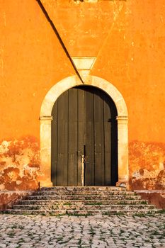 Detail of wooden door in bright orange textured wall and stone stairs