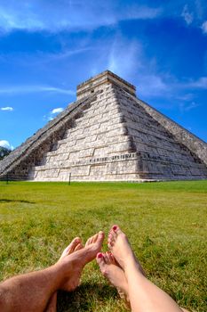 Pyramid Castillo in Chichen itza and legs of couple relaxing on grass, Mexico