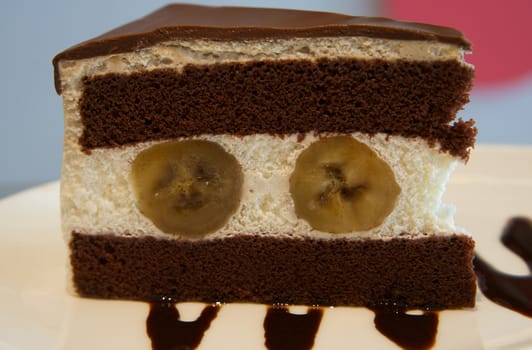 Delicious banana chocolate cake on white plate on table in restaurant.