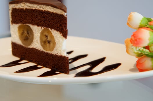 Delicious banana chocolate cake on white plate on table in restaurant.