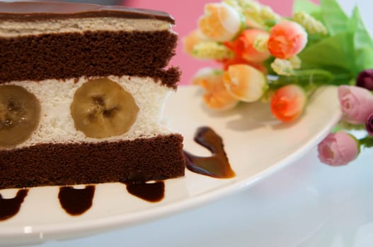 Delicious banana chocolate cake on white plate on table in restaurant.