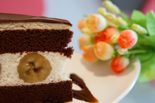 Delicious banana chocolate cake on white plate on table in restaurant.