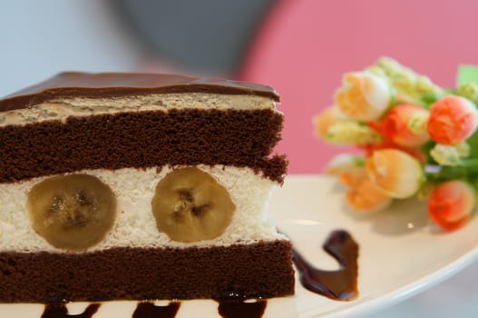 Delicious banana chocolate cake on white plate on table in restaurant.