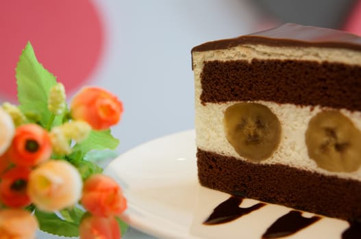 Delicious banana chocolate cake on white plate on table in restaurant.