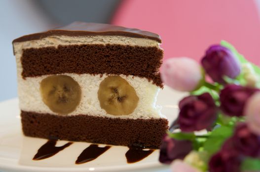 Delicious banana chocolate cake on white plate on table in restaurant.