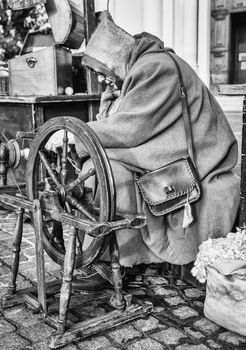 Elderly woman uses the cocoons of silkworms to spin using an old spinning wheel of wood.