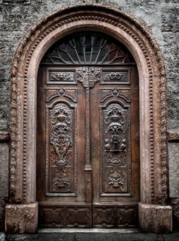 Old wooden gate with stone vault engraved with demonic figures.