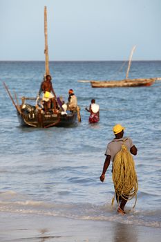 Stone Town (Zanzibar), Tanzania - January 6, 2016: A dhow (traditional sailboat) in the background and a crowded fishing boat and fishman in the foreground in the Indian Ocean just off the island of Zanzibar, Nungwi