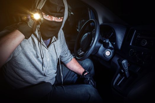 Car Thief with Flashlight Inside Stolen Car at Night. Car Insurance and Protection Concept.