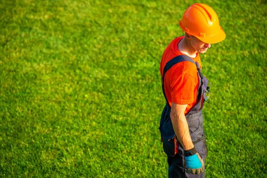 Caucasian Landscaping Contractor in Orange Helmet on the Grassy Field. Gardening and Landscaping Worker.