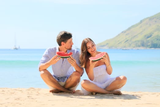 Cheerful couple eating watermelon at sea beach