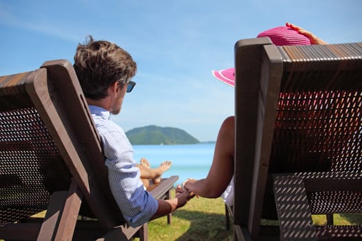 Couple enjoying vacation sitting on chairs at beach in luxury resort