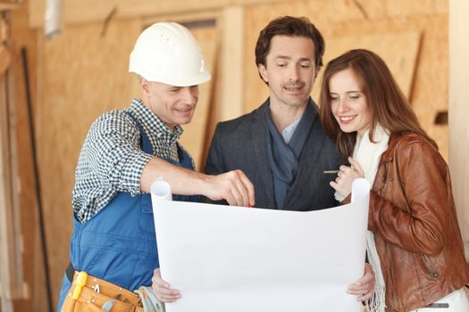 Worker shows house design plans to a young couple at construction site