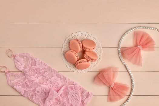 Overhead woman essentials fashion wedding accessories set. Lace pink gloves, macarons french dessert, pearl necklace, bows.Creative bride set, vanilla wooden background. Romantic, still life.Top view