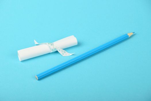 White small paper scroll note with ribbon and pencil on tender blue background