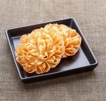 Crispy Lotus Blossom Cookie on black dish ("Dok Jog" in Thai made from flour, coconut milk, sugar, salt, sesame)