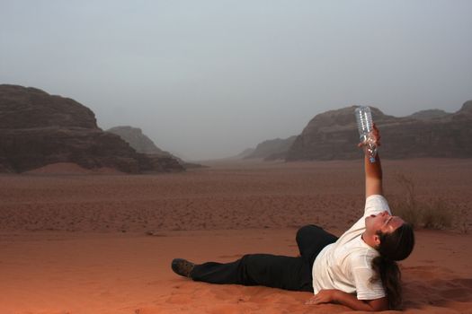 Desperate man in the desert drinking last drops of water from an empty bottle