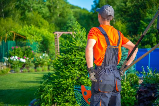 Ready to Work Gardener. Caucasian Gardener with Garden Tools is About to Start His Work in the Beautiful Garden.