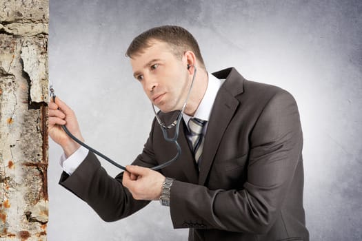 Businessman with stethoscope hearing wall on grey background