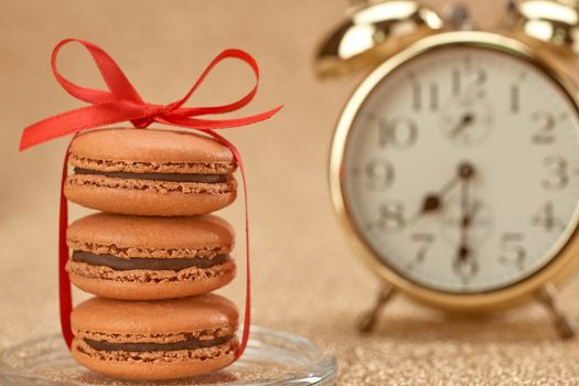 Macarons french dessert, Gold stylish alarm clock, breakfast time, red ribbon. Vintage retro romantic style. Unusual creative art greeting card. Shiny elegant luxury background, bokeh, copyspace
