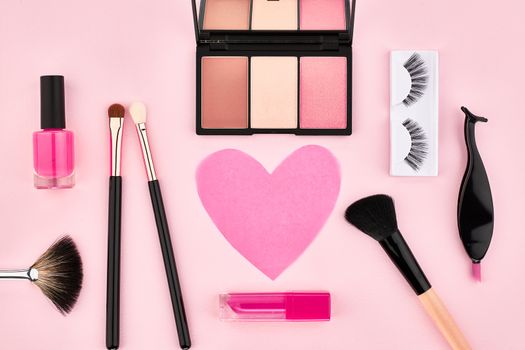 Overhead Still life, fashion woman essentials cosmetics. Beauty makeup accessories. Lipstick, brushes, eyeshadow, false eyelashes, heart. Unusual creative set. Pink background, top view