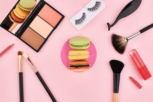 Overhead Still life, fashion woman essentials cosmetics. Beauty makeup accessories.Macarons french dessert. Lipstick, brushes, eyeshadow, false eyelashes.Unusual creative set.Pink background, top view
