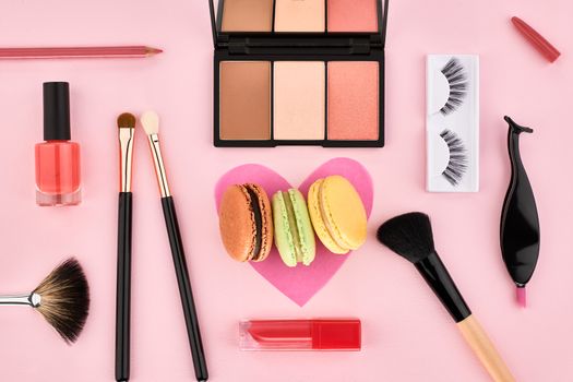 Overhead Still life, fashion woman essentials cosmetics. Beauty makeup accessories.Macarons french dessert. Lipstick, brushes, eyeshadow, false eyelashes.Unusual creative set.Pink background, top view
