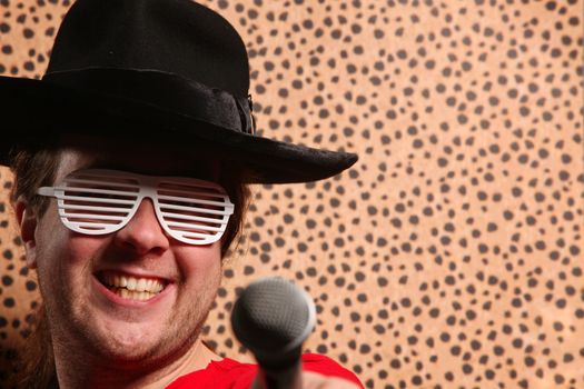 Crazy rock and roller singer with a big black hat, party glasses in front of a cheetah skin background