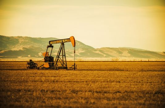 Aged Oil Pump on Colorado Prairie with Mountain Hills in the Background. Oil Industry Theme.