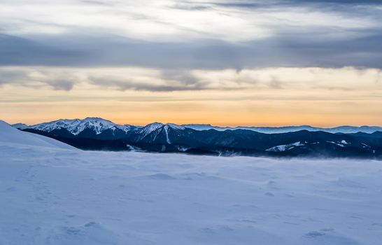 Evening winter landscape snowy peaks. Snow dust. Dusk. Orange sky, purple clouds and snow. True colors.