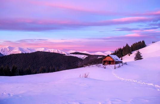 Romantic landscape of lonely wooden hut in the pink light of dawn. On background snowy mountain ridge.
