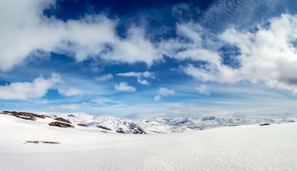 Panoramic view of mountain landscape. Pure white snow field. Blue sky, white clouds. Norway.